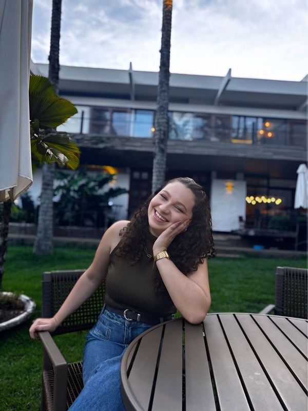 Eloisa Calvinato sorrindo em um ambiente externo tranquilo
